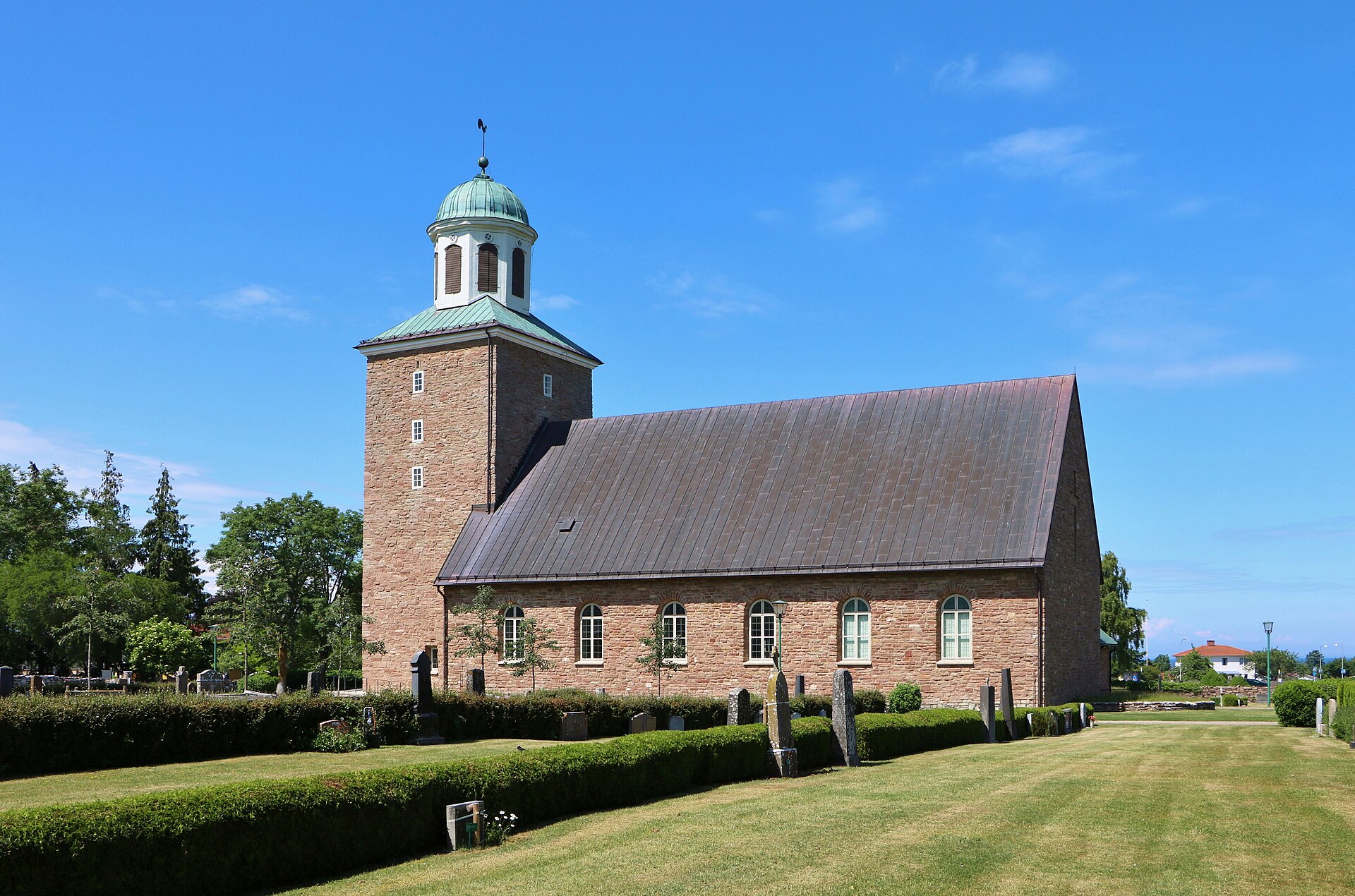 Köpings kyrka, stenkyrka med torn mot sommarhimmel.