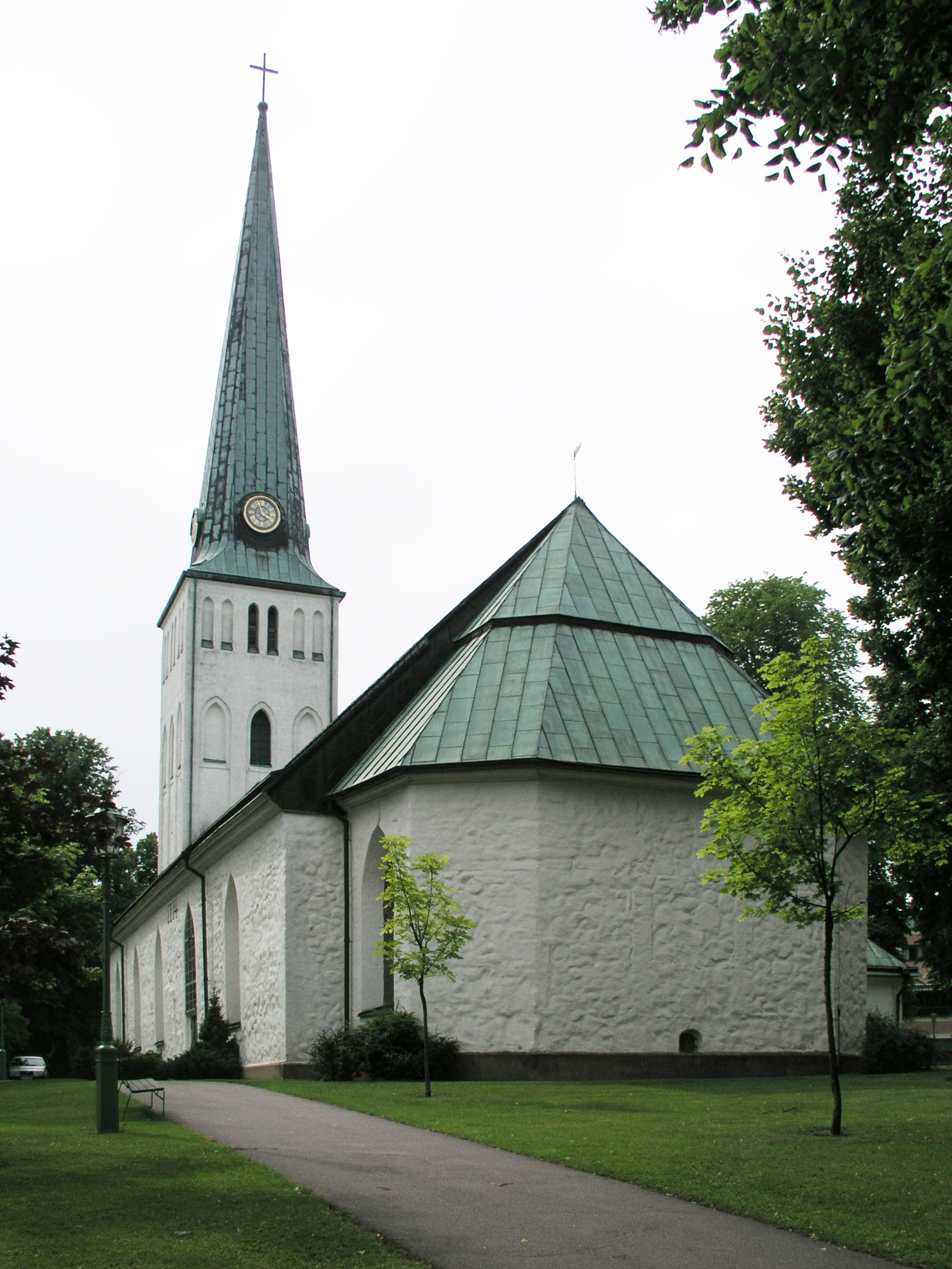 Motala kyrka, vit kyrka med torn mot sommarhimmel.